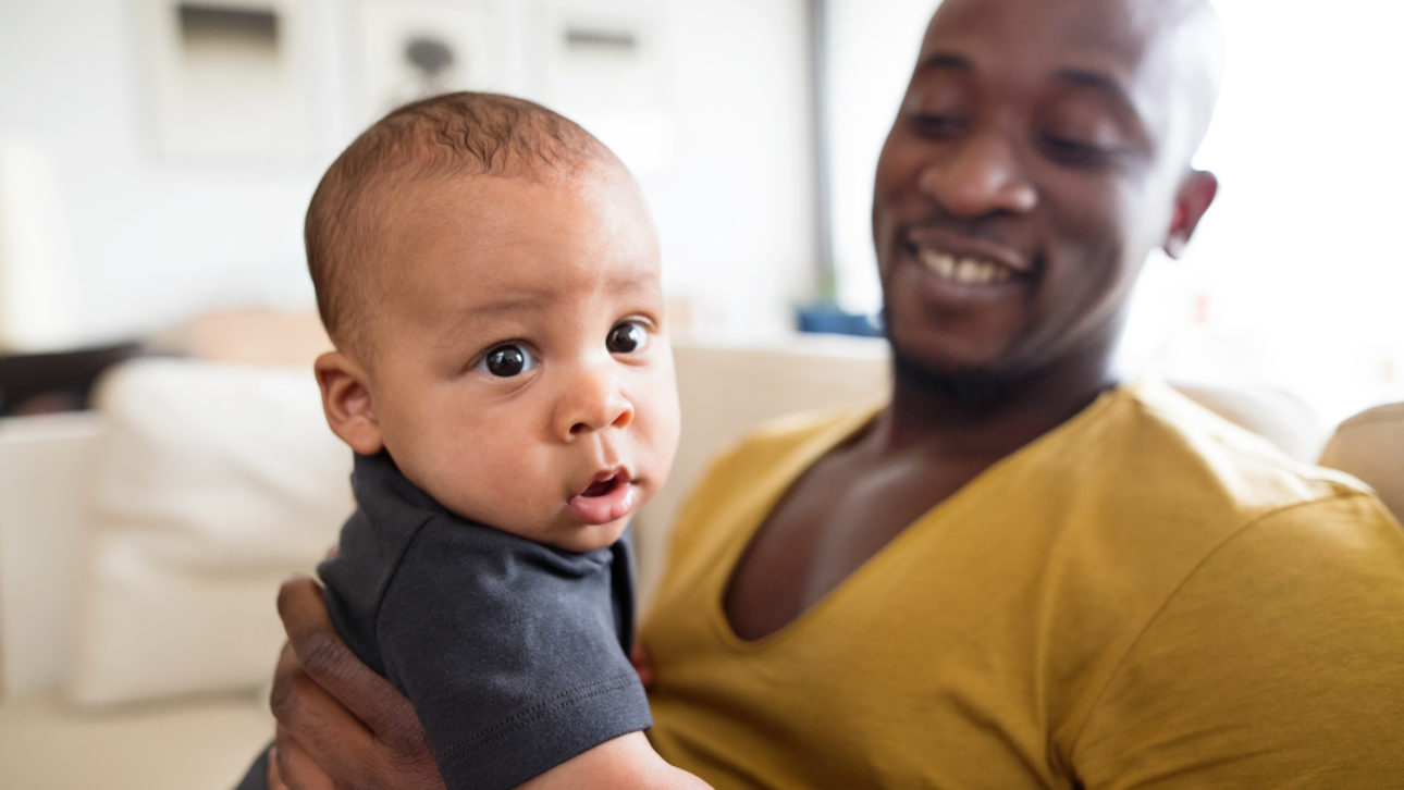 Young afro-american father at home holding his cute baby son in his arms