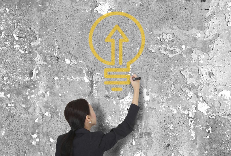 Woman drawing on wall. Studer Institute Light Bulb logo on the wall