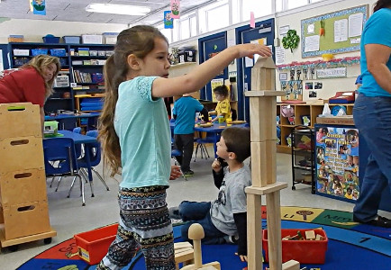 Little girl in a classroom building a structure with wooden blocks